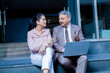 © GAJENDRRA BHATI  - Indian senior corporate businessman with his female colleague discussing about company growth using laptop while sitting on office stairs.