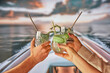 © Lustre Art Group  - Group of people, friends relaxing on yacht in the evening, hands clinking glasses with cocktails, enjoying tranquil nature and sunset. Concept of summer, vacation, travelling, relaxation