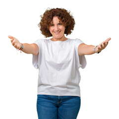 Wall Mural - Beautiful middle ager senior woman wearing white t-shirt over isolated background looking at the camera smiling with open arms for hug. Cheerful expression embracing happiness.