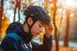 © VisualProduction - A man wearing a black cycling helmet adjusts his helmet with both hands. He is dressed in a black jacket and is outdoors with a blurred background of trees.