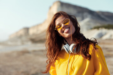 Canvas Print - Woman in yellow shirt and sunglasses standing on beach overlooking distant mountain on sunny day