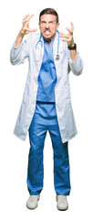 Wall Mural - Handsome doctor man wearing medical uniform over isolated background Shouting frustrated with rage, hands trying to strangle, yelling mad