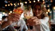 © LifeMedia - Two individuals clink glasses filled with refreshing beverages amidst a lively restaurant bar setting adorned with warm bokeh lights, creating a vibrant social atmosphere.