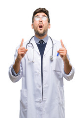 Poster - Young handsome doctor man over isolated background amazed and surprised looking up and pointing with fingers and raised arms.