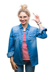 Canvas Print - Young beautiful blonde woman wearing glasses over isolated background smiling and confident gesturing with hand doing size sign with fingers while looking and the camera. Measure concept.