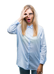 Canvas Print - Young beautiful blonde business woman wearing glasses over isolated background doing ok gesture shocked with surprised face, eye looking through fingers. Unbelieving expression.