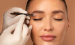 © Home-stock - Hand holding tweezers and shaping eyebrows to young European woman, beautician plucking brow hairs of lady over beige background, closeup