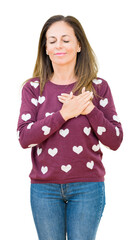 Poster - Beautiful middle age woman wearing hearts sweater over isolated background smiling with hands on chest with closed eyes and grateful gesture on face. Health concept.