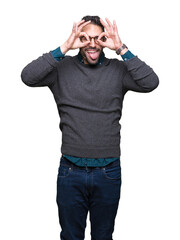 Canvas Print - Young handsome man wearing glasses over isolated background doing ok gesture like binoculars sticking tongue out, eyes looking through fingers. Crazy expression.