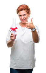 Canvas Print - Senior caucasian woman holding degree certificate over isolated background happy with big smile doing ok sign, thumb up with fingers, excellent sign