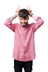 Poster - Young handsome man wearing pink shirt over isolated background Posing funny and crazy with fingers on head as bunny ears, smiling cheerful