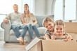 © CoetzeeRising/peopleimages.com - Girls, portrait and box in living room for game, play and fun in family home on weekend. Sisters, children and together in lounge with parents for development, moving and happy for new house