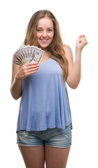 Wall Mural - Young blonde woman holding dollars screaming proud and celebrating victory and success very excited, cheering emotion