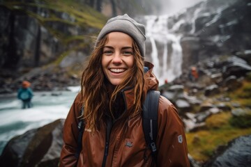 Wall Mural - Portrait of a happy woman in her 20s donning a durable down jacket over backdrop of a spectacular waterfall