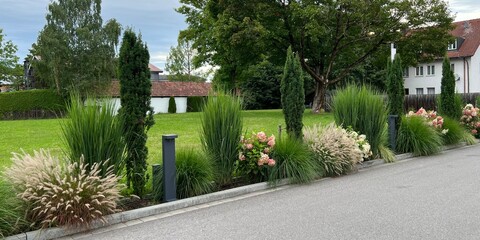 Wall Mural - Colorful flower beds with evergreen yews, green grasses and pink and white flowering panicle hydrangeas next to the entrance to a parking lot.