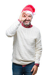 Canvas Print - Middle age hoary senior man wearing christmas hat over isolated background doing ok gesture with hand smiling, eye looking through fingers with happy face.