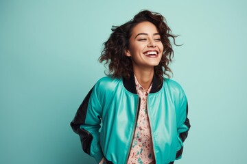 Wall Mural - Portrait of a jovial woman in her 30s wearing a trendy bomber jacket while standing against pastel teal background