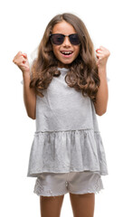 Canvas Print - Brunette hispanic girl wearing sunglasses celebrating surprised and amazed for success with arms raised and open eyes. Winner concept.