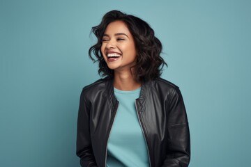 Wall Mural - Portrait of a jovial indian woman in her 30s wearing a trendy bomber jacket in front of soft blue background