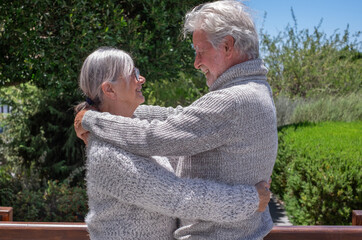 Senior couple enjoying a beautiful day outdoors, smiling and embracing each other. Elderly retirees reflecting their deep bond and affection. Grey haired joyful caucasian people in nature's greenery