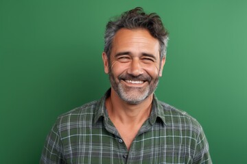 Wall Mural - Portrait of a smiling man in his 50s wearing a comfy flannel shirt on soft green background