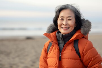 Wall Mural - Portrait of a blissful asian woman in her 60s donning a durable down jacket on sandy beach background