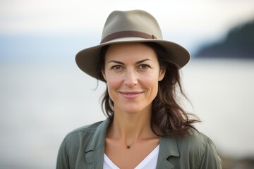 Wall Mural - Portrait of a smiling woman in her 40s donning a classic fedora isolated in serene seaside background