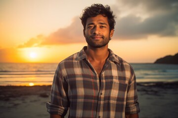 Canvas Print - Portrait of a satisfied indian man in his 20s dressed in a relaxed flannel shirt on stunning sunset beach background