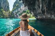 © Kishore Newton - A traveler in a straw hat admires stunning limestone cliffs and turquoise waters from a wooden boat in a tropical paradise lagoon.