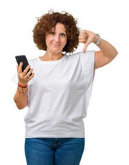 Wall Mural - Middle ager senior woman using and texting with smartphone over isolated background with angry face, negative sign showing dislike with thumbs down, rejection concept