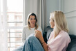 © Ilona - Two cheerful beautiful blonde women are chatting while sitting on the sofa in the living room.