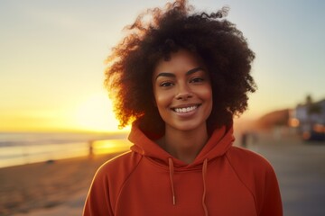 Wall Mural - Portrait of a grinning afro-american woman in her 20s wearing a thermal fleece pullover isolated on vibrant beach sunset background