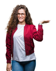 Poster - Beautiful brunette curly hair young girl wearing jacket and glasses over isolated background smiling cheerful presenting and pointing with palm of hand looking at the camera.