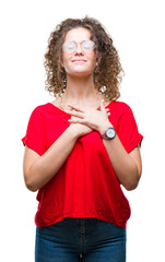 Sticker - Beautiful brunette curly hair young girl wearing glasses over isolated background smiling with hands on chest with closed eyes and grateful gesture on face. Health concept.