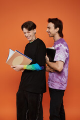 Wall Mural - Two LGBTQIA friends in stylish outfits laugh and enjoy each others company against an orange backdrop.