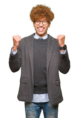 Wall Mural - Young handsome business man with afro wearing glasses celebrating surprised and amazed for success with arms raised and open eyes. Winner concept.