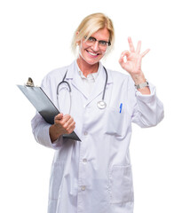 Poster - Middle age blonde doctor woman holding clipboard over isolated background doing ok sign with fingers, excellent symbol