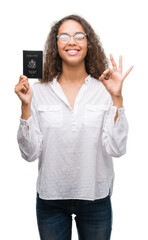 Sticker - Young hispanic woman holding passport of United States of America doing ok sign with fingers, excellent symbol