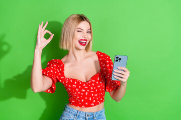 Wall Mural - Photo of gorgeous cheerful cute girl wear red trendy clothes pomade hold iphone okey sign isolated on green color background