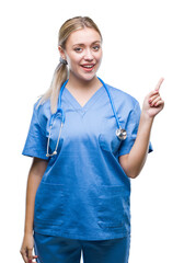 Poster - Young blonde surgeon doctor woman over isolated background with a big smile on face, pointing with hand and finger to the side looking at the camera.