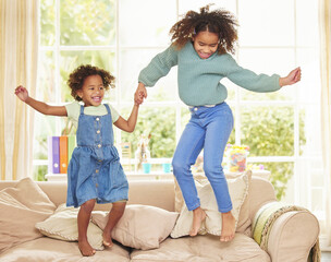 Poster - Children, girls and holding hands for jumping in home, bonding and game for fun or love in childhood. Sisters, kids and playing together on couch in living room, happiness and weekend for support