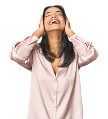 Wall Mural - Simple portrait of a young Latina laughs joyfully keeping hands on head. Happiness concept.