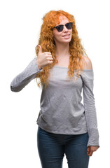 Canvas Print - Young redhead woman wearing sunglasses happy with big smile doing ok sign, thumb up with fingers, excellent sign