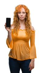 Sticker - Young redhead woman showing smartphone with a confident expression on smart face thinking serious