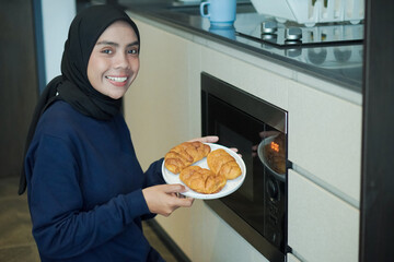 Wall Mural - A woman is smiling and holding a plate of food in front of a microwave