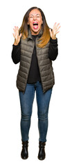 Wall Mural - Beautiful middle age woman wearing winter vest celebrating mad and crazy for success with arms raised and closed eyes screaming excited. Winner concept