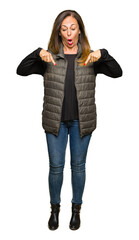 Wall Mural - Beautiful middle age woman wearing winter vest Pointing down with fingers showing advertisement, surprised face and open mouth