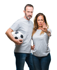 Wall Mural - Middle age hispanic couple holding football soccer ball over isolated background with open hand doing stop sign with serious and confident expression, defense gesture