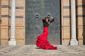 Canvas Print - Young, beautiful, brunette woman in black shirt and red skirt, dancing flamenco in front of an old, black metal door. Flamenco concept, dance, art, typical Spanish.