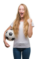 Poster - Blonde teenager woman holding soccer football ball screaming proud and celebrating victory and success very excited, cheering emotion